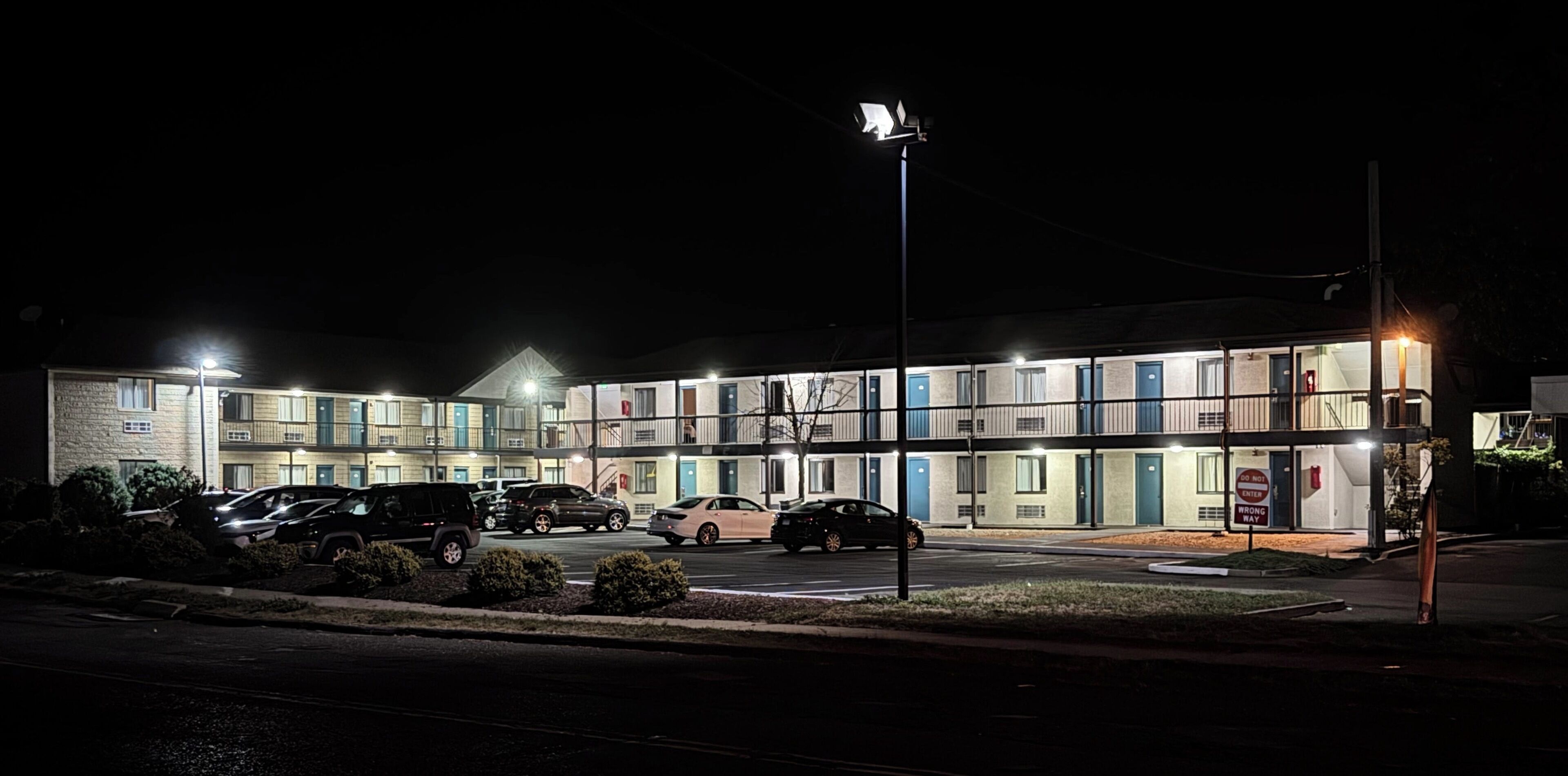A multi-story motel with several rooms, a parking lot, and a streetlight.