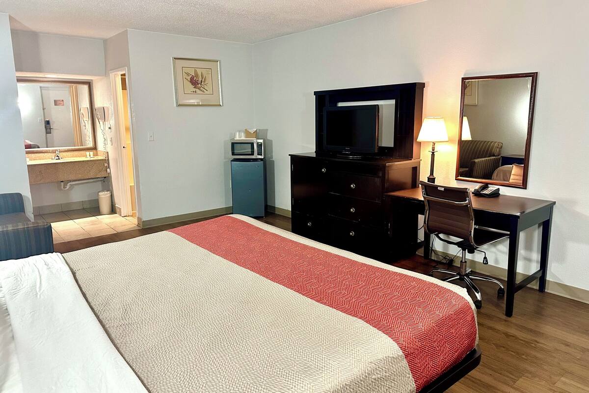 A hotel room with a bed, a desk, a chair, a television, a microwave, and a small refrigerator.