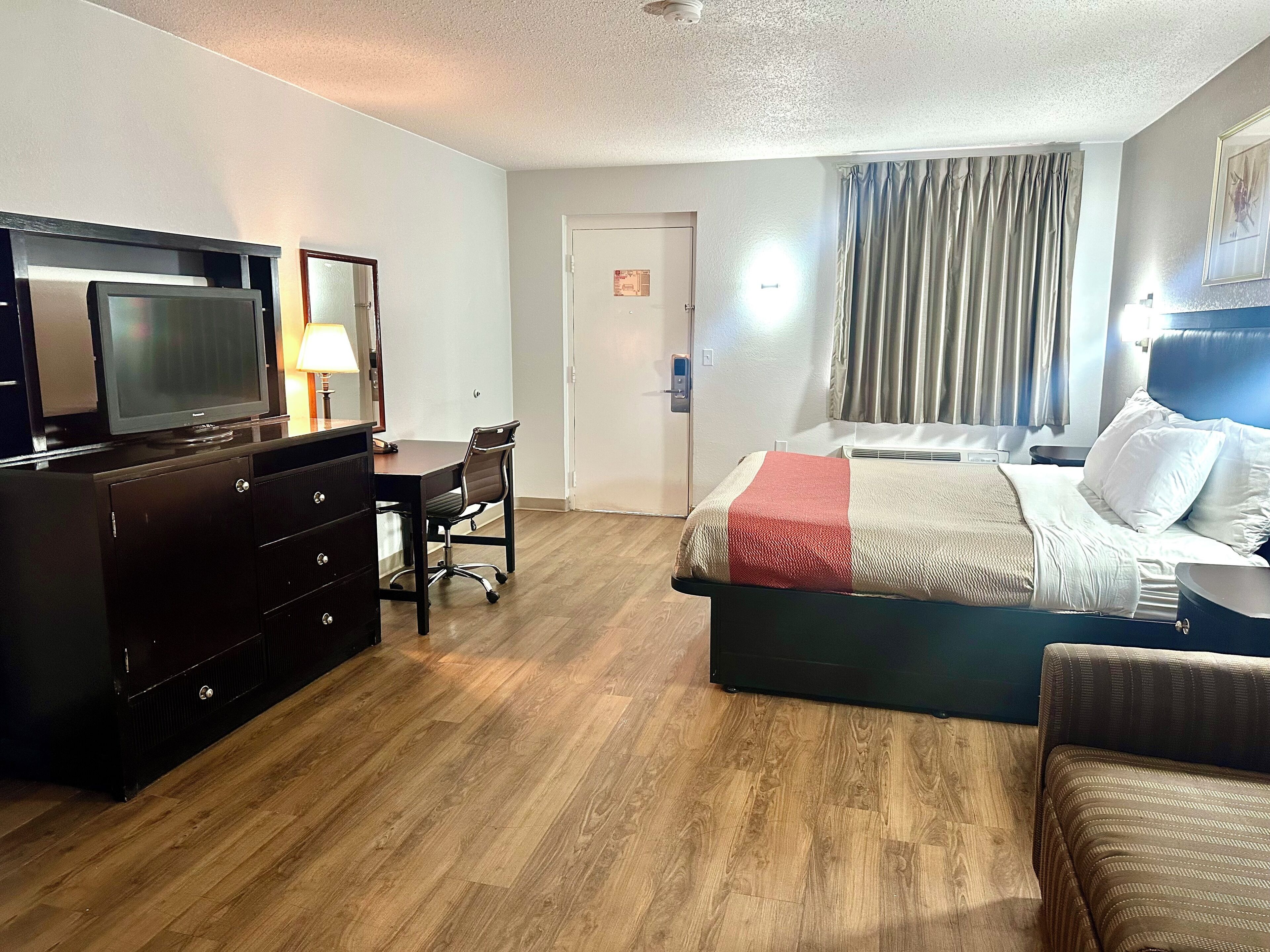 Una habitación de hotel con cama, escritorio con silla, televisión y cómoda.