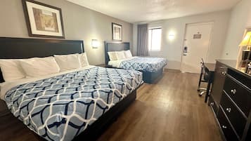A hotel room with two beds, wooden flooring, a desk, and a dresser.
