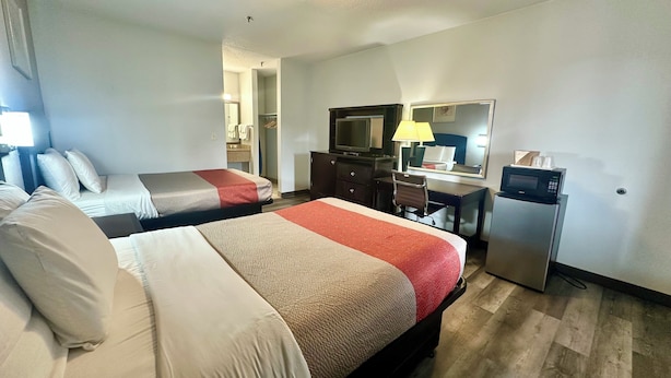 Ein Hotelzimmer mit zwei Betten, einem Schreibtisch, einem Sessel, einem Fernseher, einem Spiegel und einem Kühlschrank.