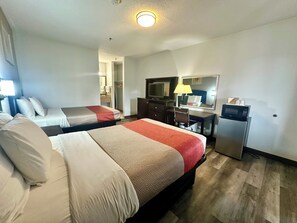 A hotel room with two beds, a desk, a chair, a television, a mirror, and a refrigerator.