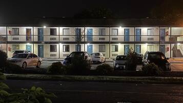 Un motel à étages, avec une rangée de chambres à chaque étage, un parking où sont garées plusieurs voitures et un escalier menant aux étages supérieurs.