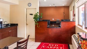 Empfangsbereich eines Red Carpet Inn mit einem Holzbüro, einer Wanduhr, einer Pflanze und einem Süßigkeitenautomaten.