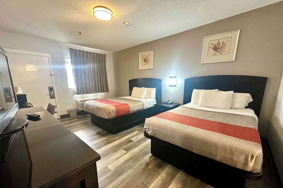 A hotel room with two beds, a desk, and a chair.