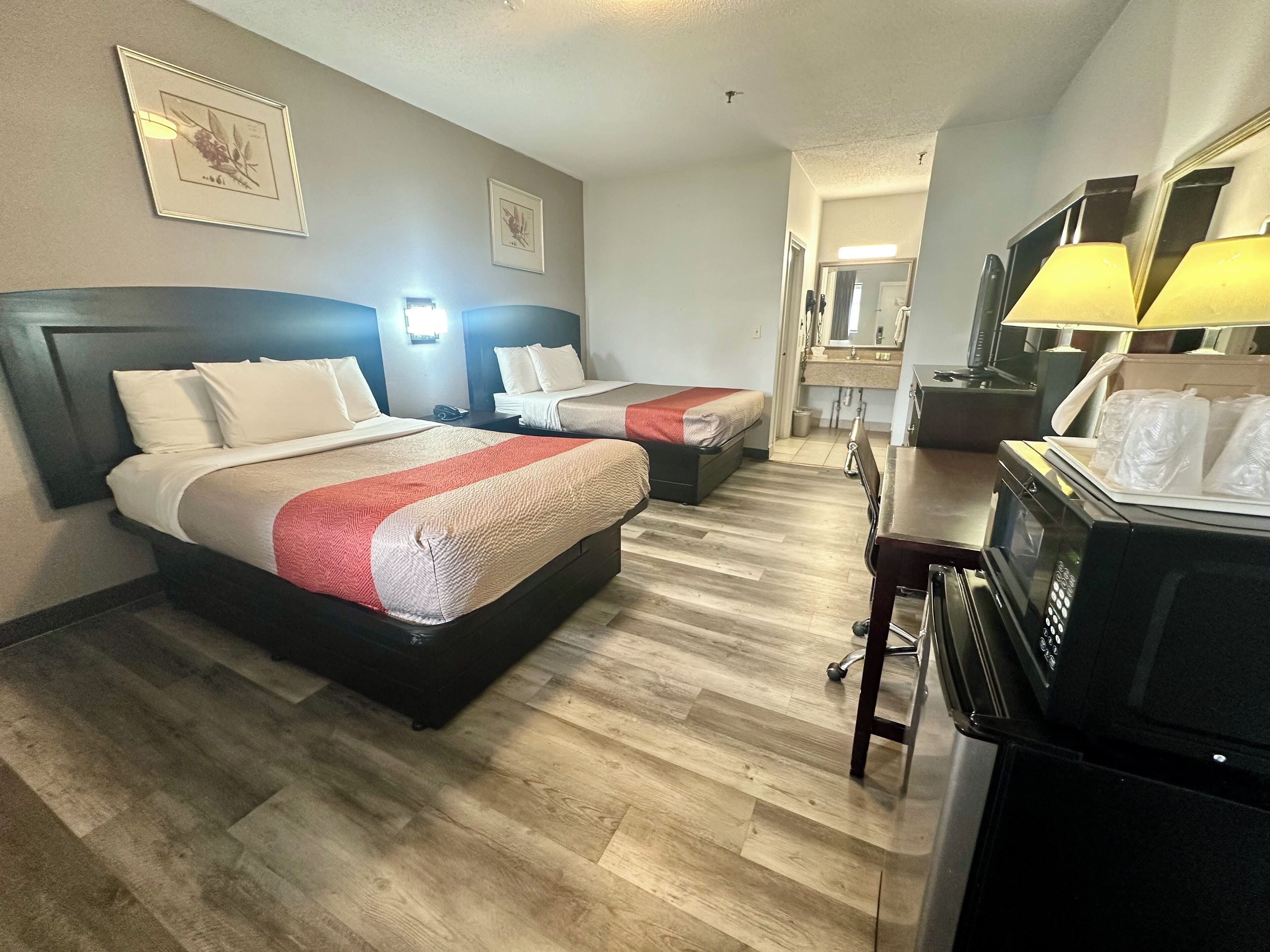 A hotel room with two beds, a kitchenette, a mirror, and a bathroom visible in the background.
