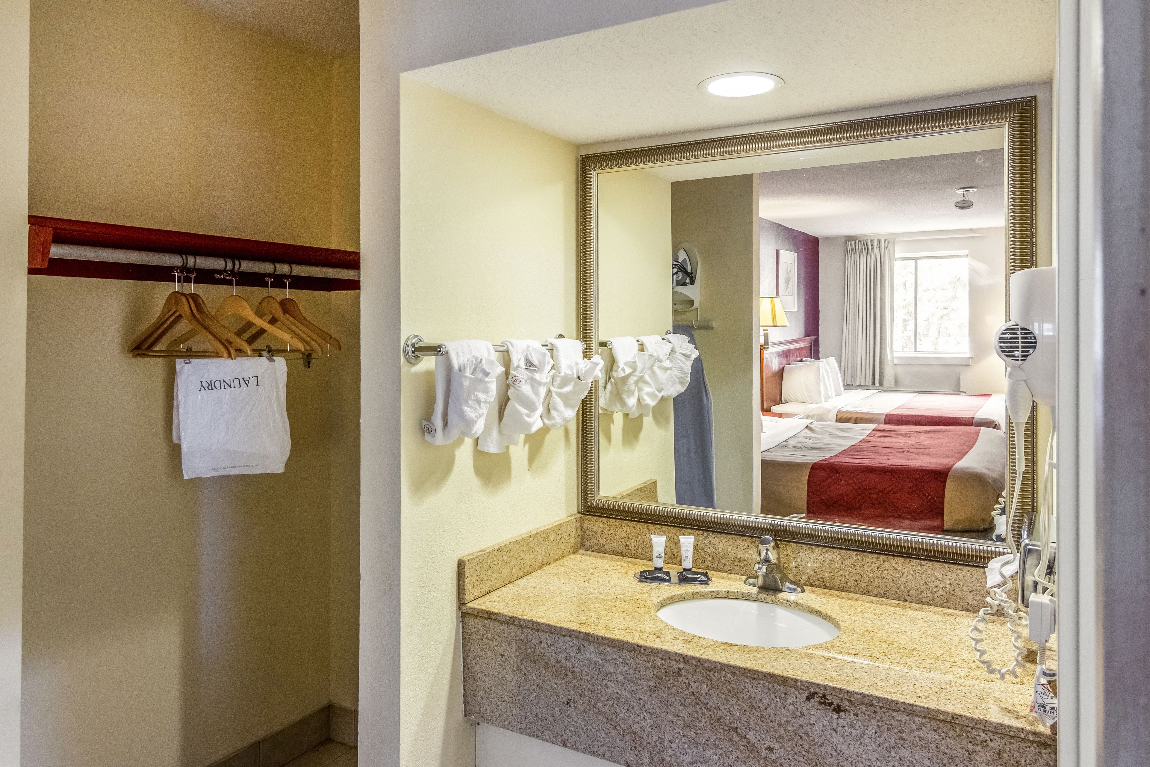A hotel bathroom with a granite countertop sink, a large mirror, and a towel rack with hangers.