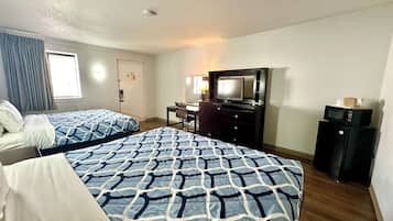 A hotel room with two beds, a desk, a television, and a refrigerator.