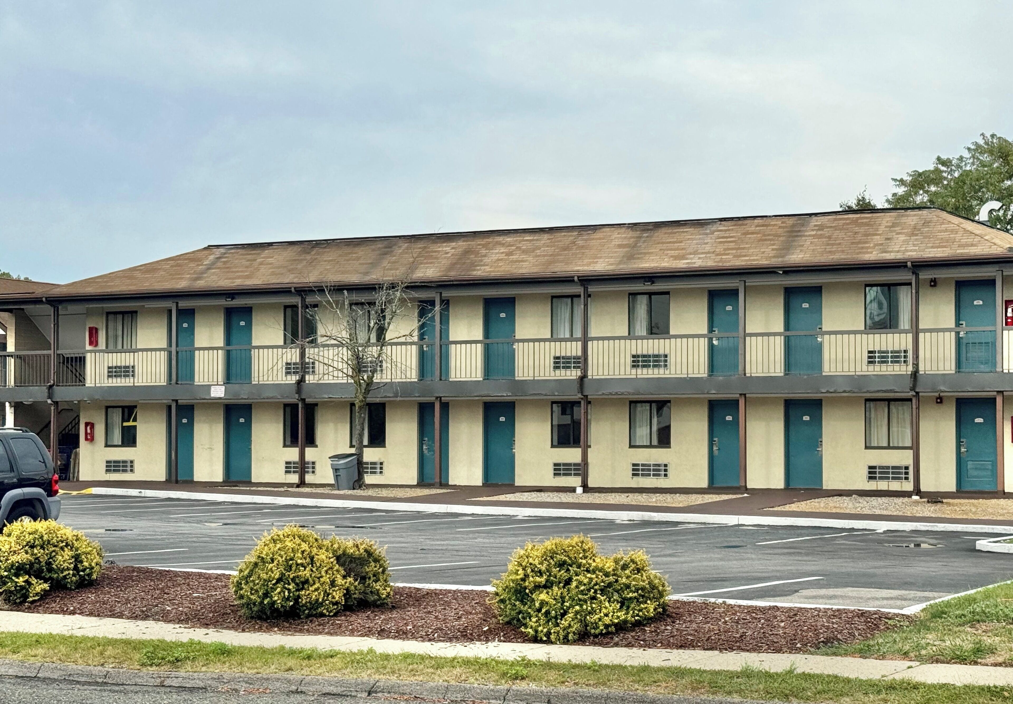 A motel with a row of rooms, a parking lot, and small bushes in front.