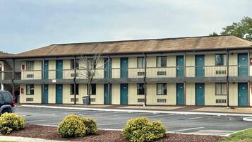 A motel with a row of rooms, a parking lot, and small bushes in front.