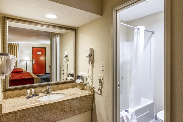 A hotel bathroom with a sink, mirror, hairdryer, and shower.