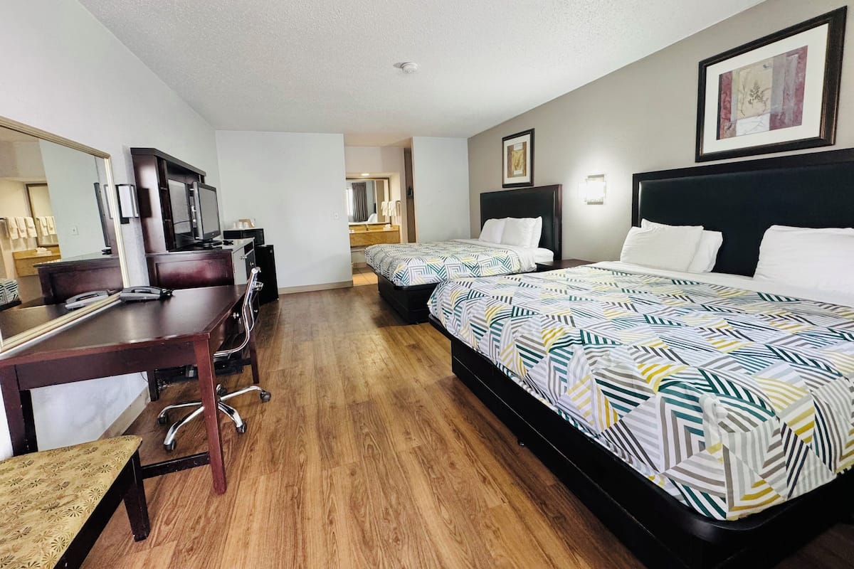A hotel room with two beds, a desk with a chair, a TV, and a large mirror.
