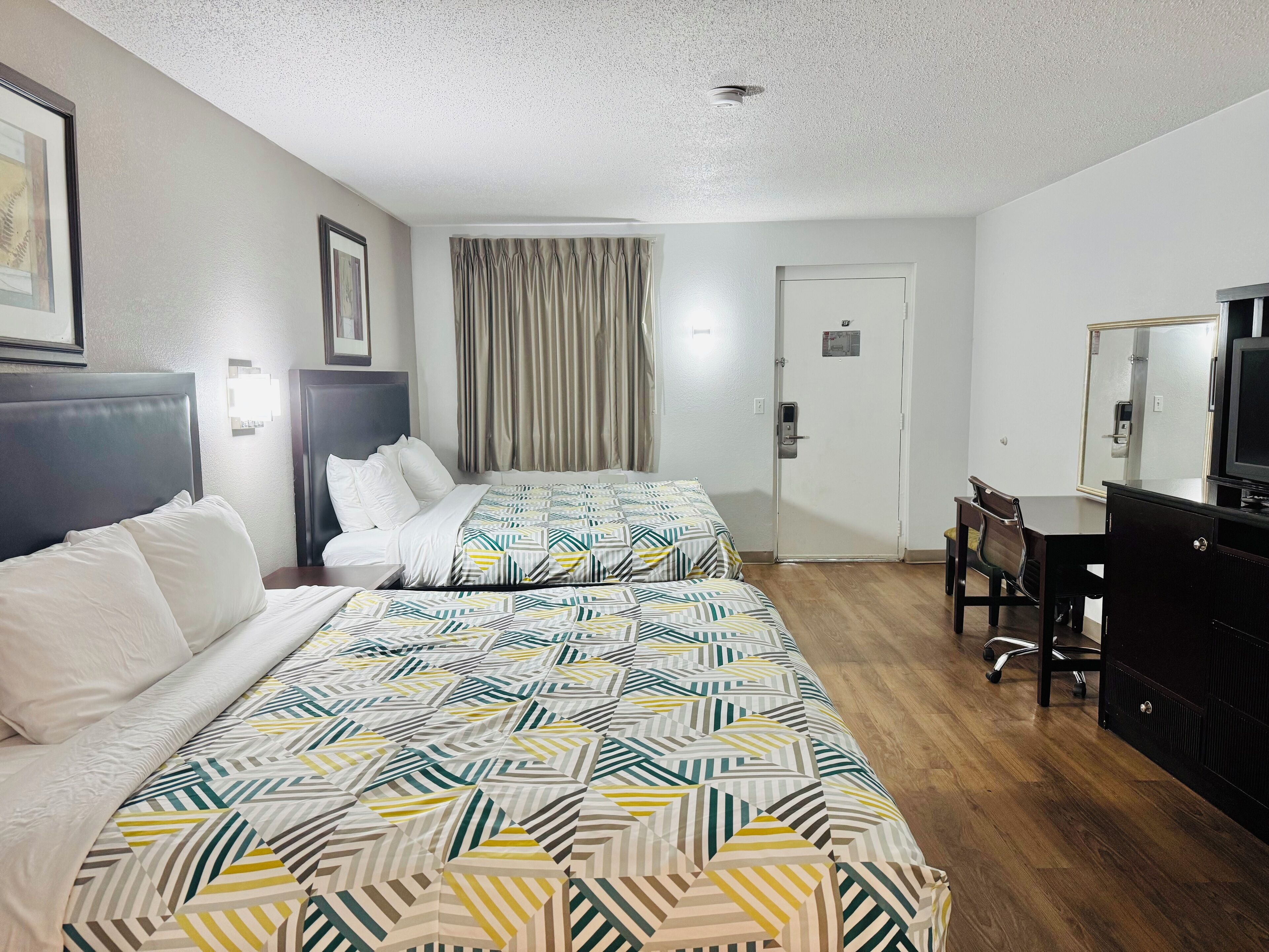 Une chambre d’hôtel avec deux lits, un bureau, une chaise, une télévision et une porte équipée d’une caméra de surveillance.