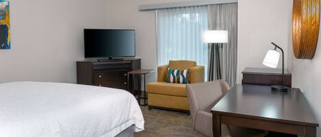 A hotel room with a bed, a desk, a chair, a television, and a lamp.