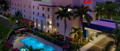 A hotel with a swimming pool, palm trees, and a neon sign.