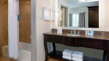 A bathroom with a bathtub, a vanity with a sink, a mirror, and a towel rack.