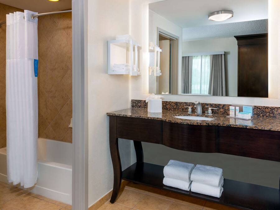 A bathroom with a bathtub, a vanity with a sink, a mirror, and a towel rack.