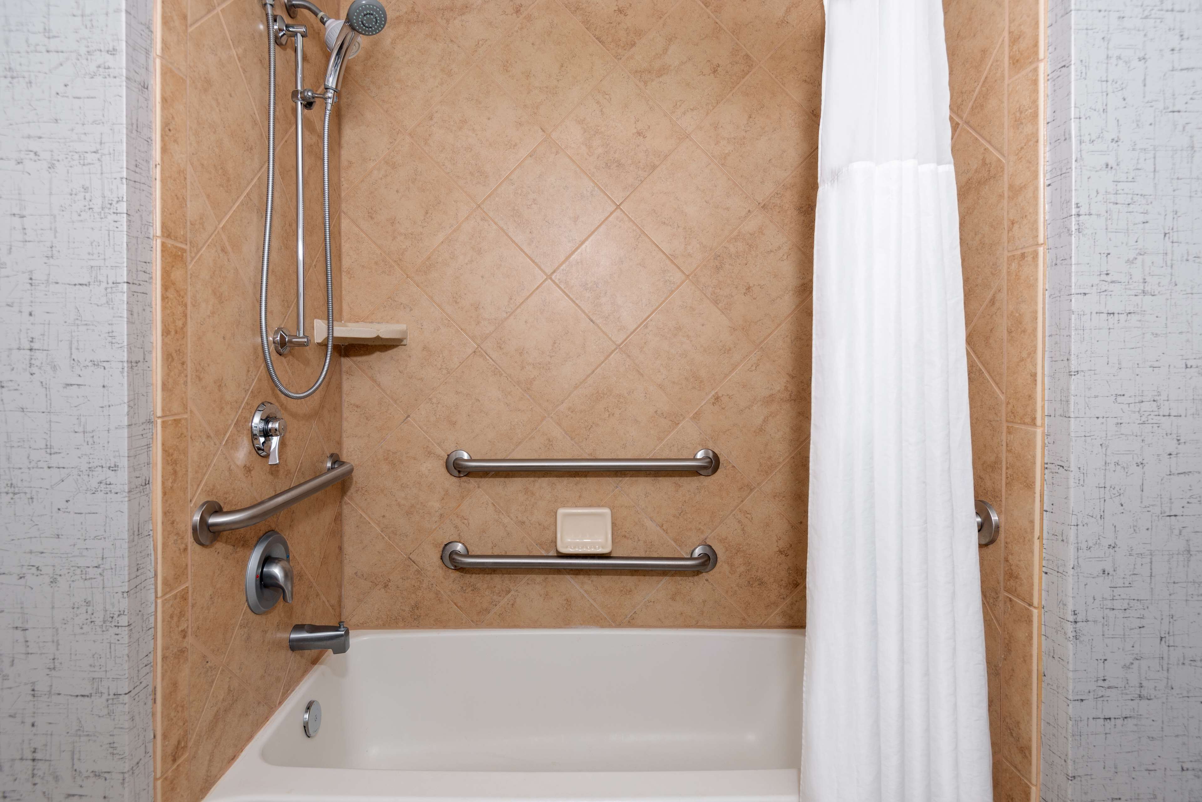 A bathroom with a bathtub, a shower, and grab bars.