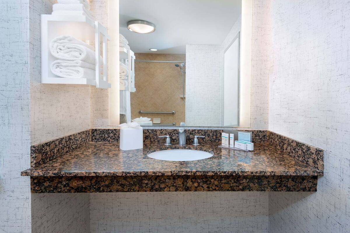 A bathroom with a granite countertop, a sink, a mirror, and a towel rack with folded towels.