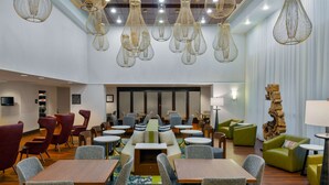 Een moderne hotellobby met zithoeken, tafels en hanglampen.