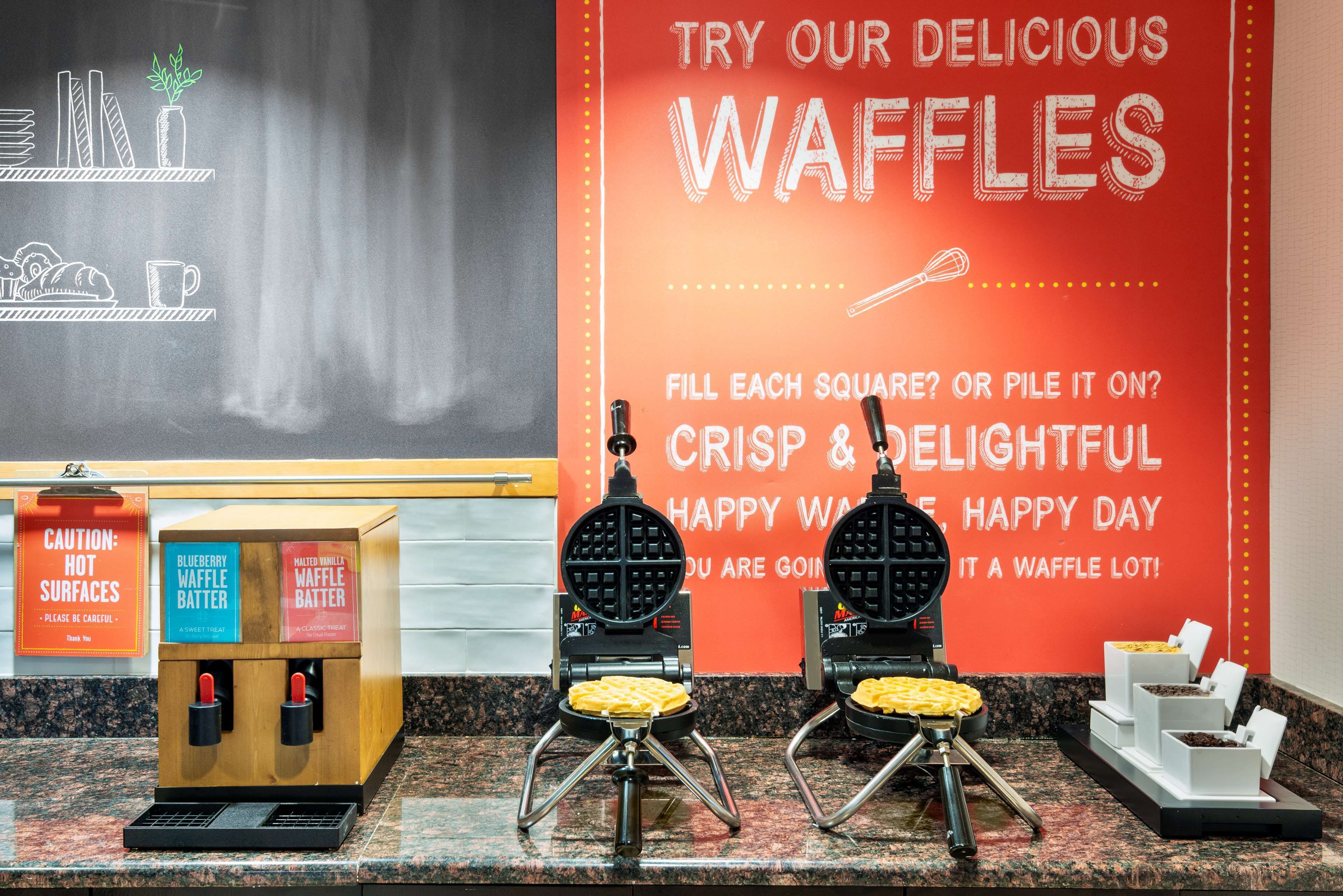 A waffle station with two waffle makers and a sign advertising waffles.