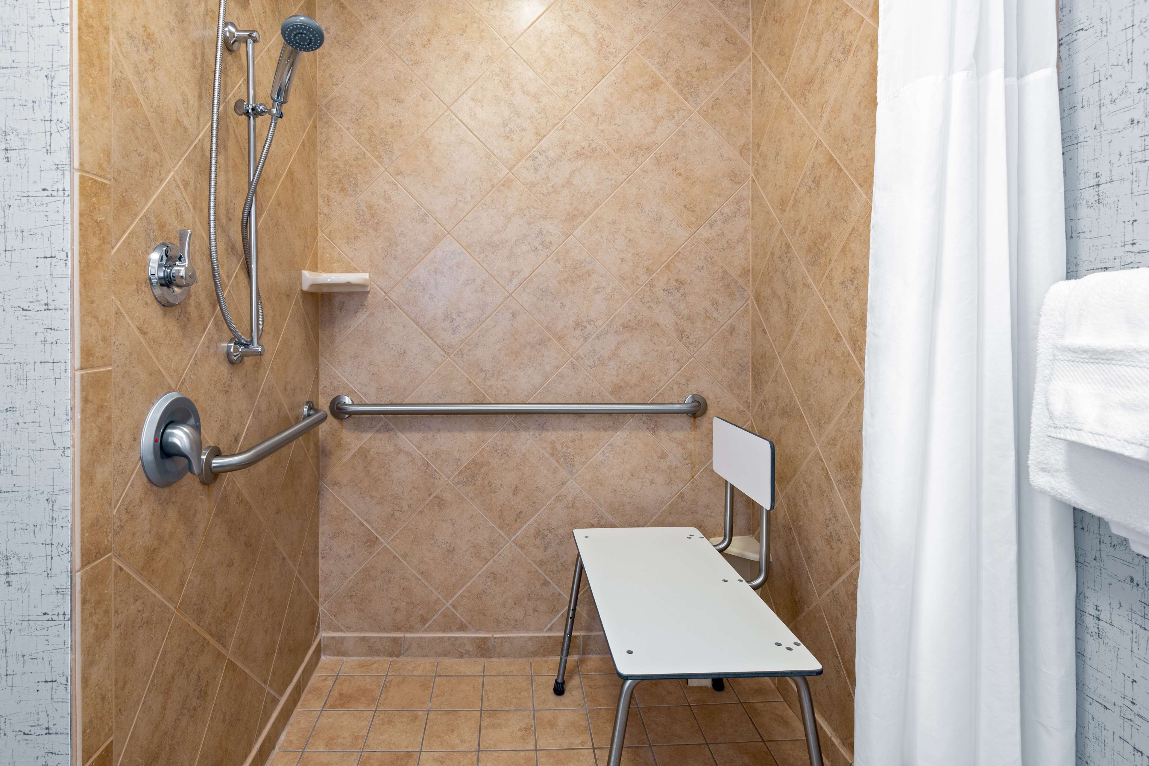 A shower area with a grab bar, a handheld showerhead, and a towel rack.
