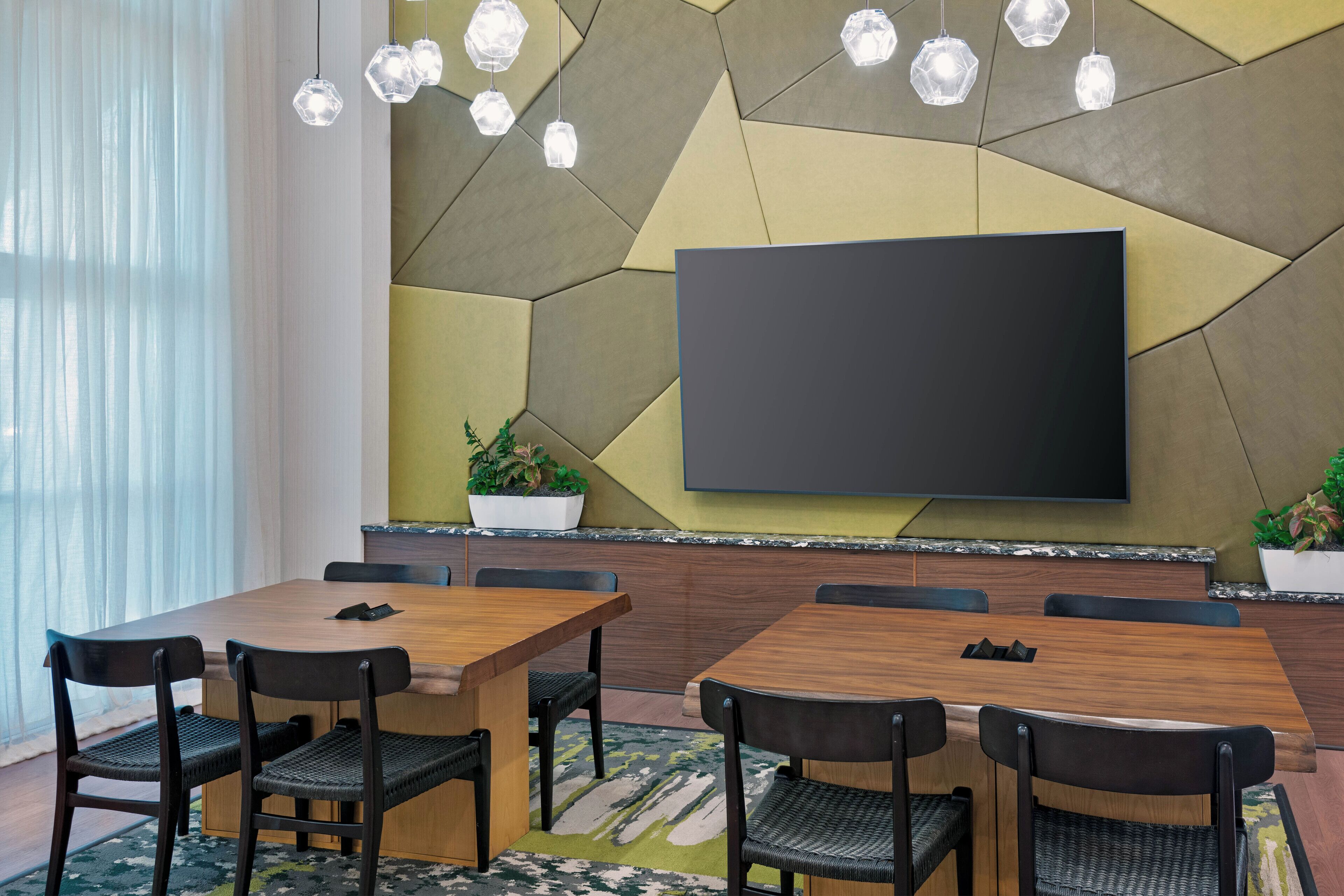 Een vergaderruimte met een groot flatscreentelevisie, een houten tafel en stoelen.