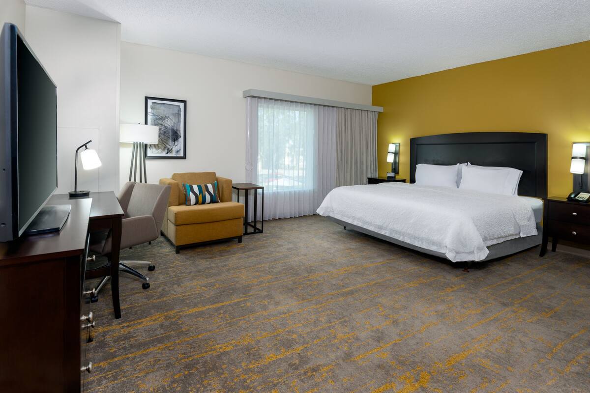 A hotel room with a bed, a desk, a chair, a TV, and a lamp.
