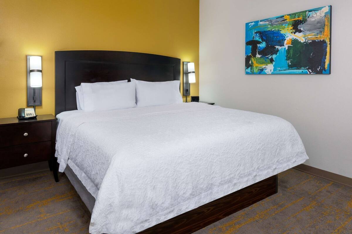 A hotel room with a large bed, bedside lamps, a nightstand, and a painting on the wall.
