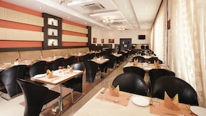 A restaurant with multiple dining tables, black chairs, and a modern ceiling design. - Regency Tuticorin by GRT Hotels (Thoothukudi)