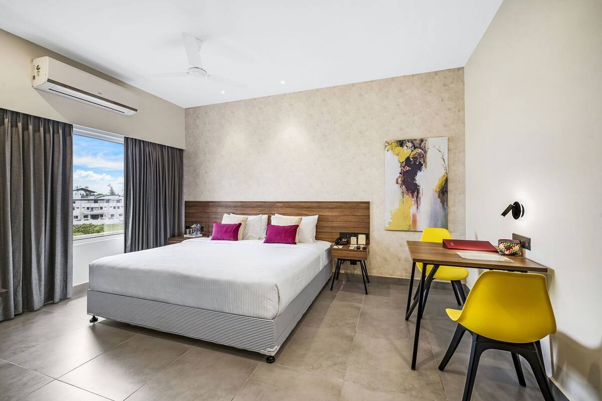 Ein Hotelzimmer mit Bett, Schreibtisch, Stuhl, Klimaanlage und einem Bild an der Wand.
