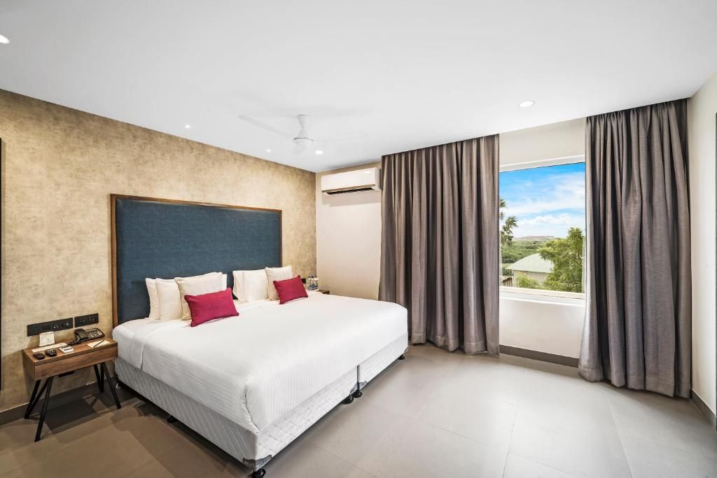 A hotel room with a large bed, a bedside table with a phone, and a view of the outdoors through the window.