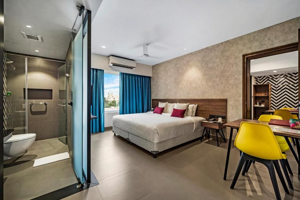 Quarto de hotel moderno com cama, escrivaninha e área de chuveiro.