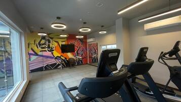 A gym with treadmills, a wall with colorful artwork, and a window providing natural light.