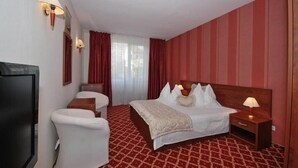 Habitación de hotel con una cama grande, un escritorio, una silla, un televisor y una ventana con cortinas.