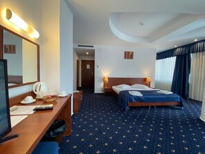 A hotel room with a bed, bedside tables, a desk with a chair, a television, and a large window with curtains. - Samaa Hotel (Bucharest)