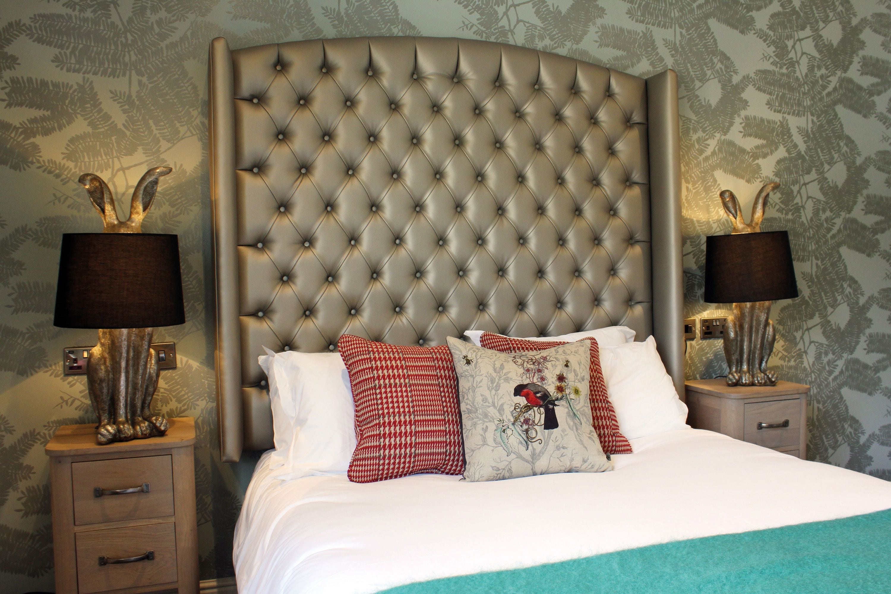 A bedroom with a tufted headboard, a bed with white linens, red and white patterned pillows, and two bedside tables with lamps.
