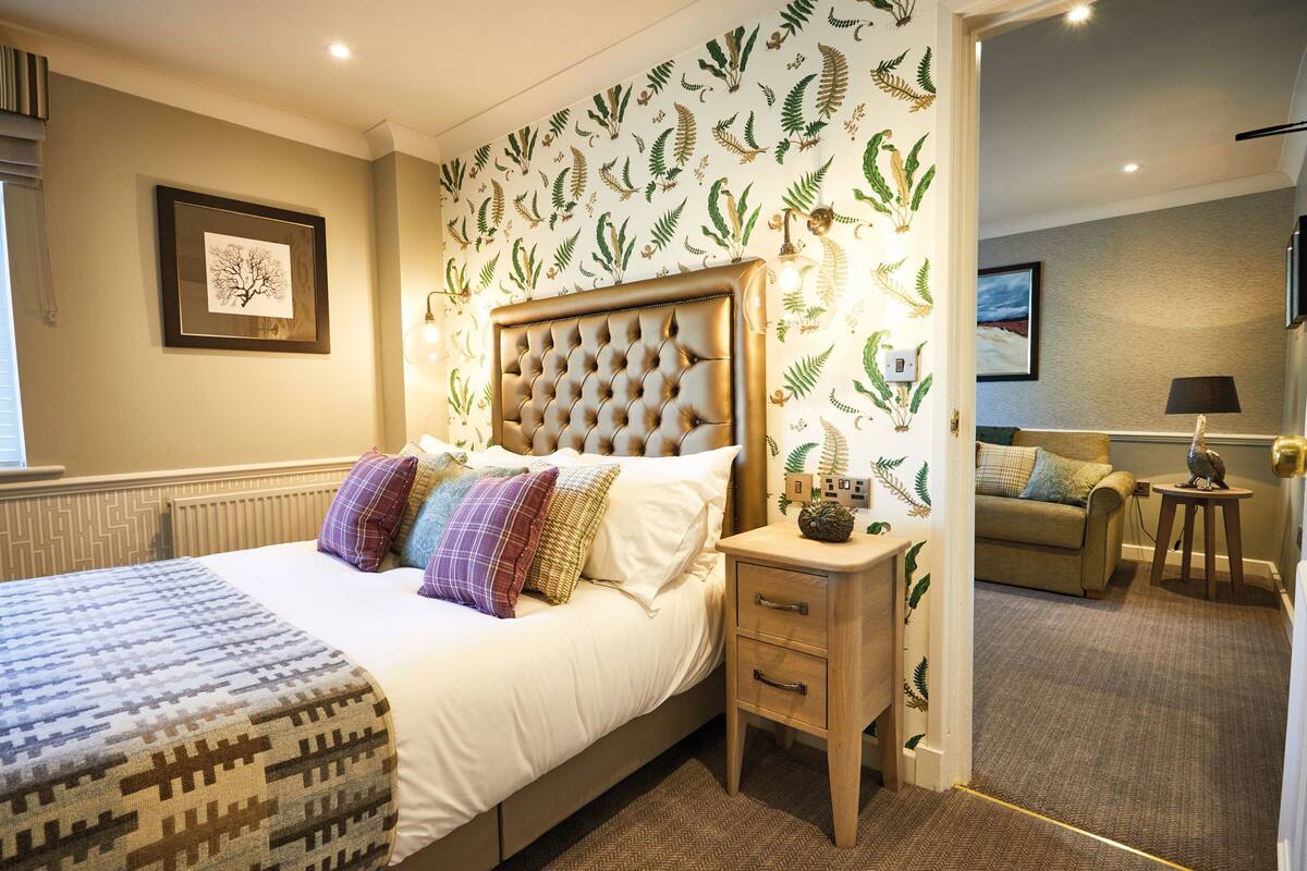 A bedroom with a bed, bedside table, and a view into another room.