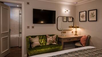 Hotelkamer met een groene fluweelzitzak, een houten bureau, een bed met een gestreept dekbedovertrek, een flatscreen televisie, een wandspiegel en ingelijste botanische prints.