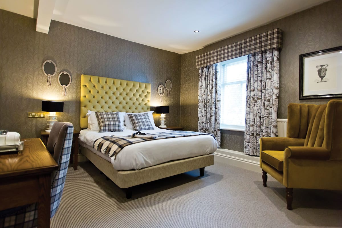 A hotel room with a large bed, a wooden desk, a chair, and a window with patterned curtains.