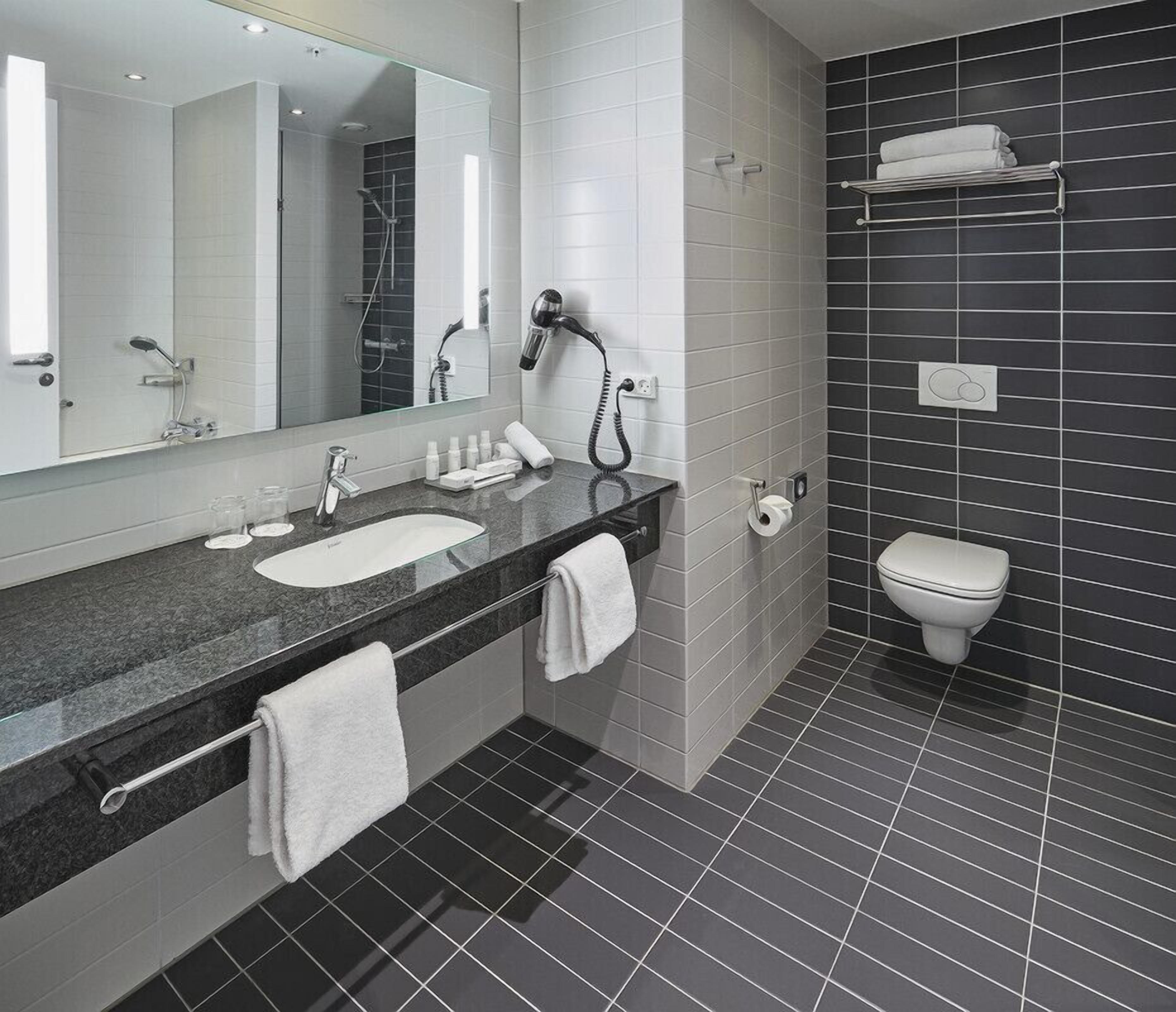A modern bathroom with a large mirror, a sink, a toilet, and a hairdryer.