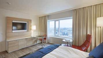 Habitación de hotel con cama, escritorio, silla, mesita y televisor montado en la pared.