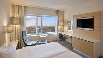 A hotel room with a bed, a desk, a chair, a TV, and a window with a city view.