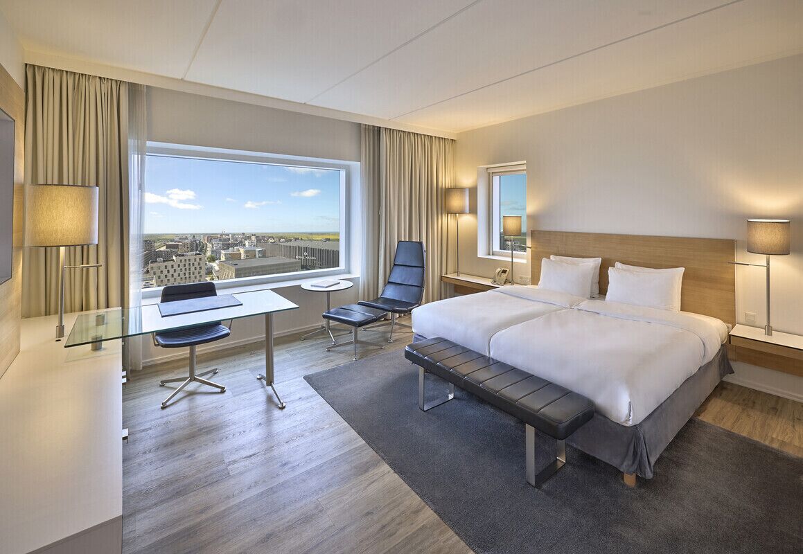 Habitación de hotel con una cama grande, un escritorio, una silla y vistas a la ciudad.