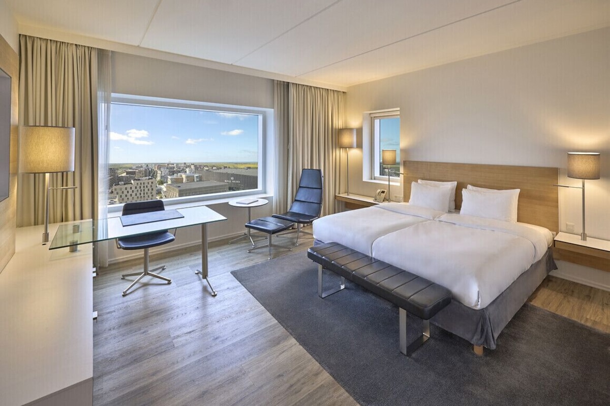 A hotel room with a large bed, a desk, a chair, and a view of the cityscape.
