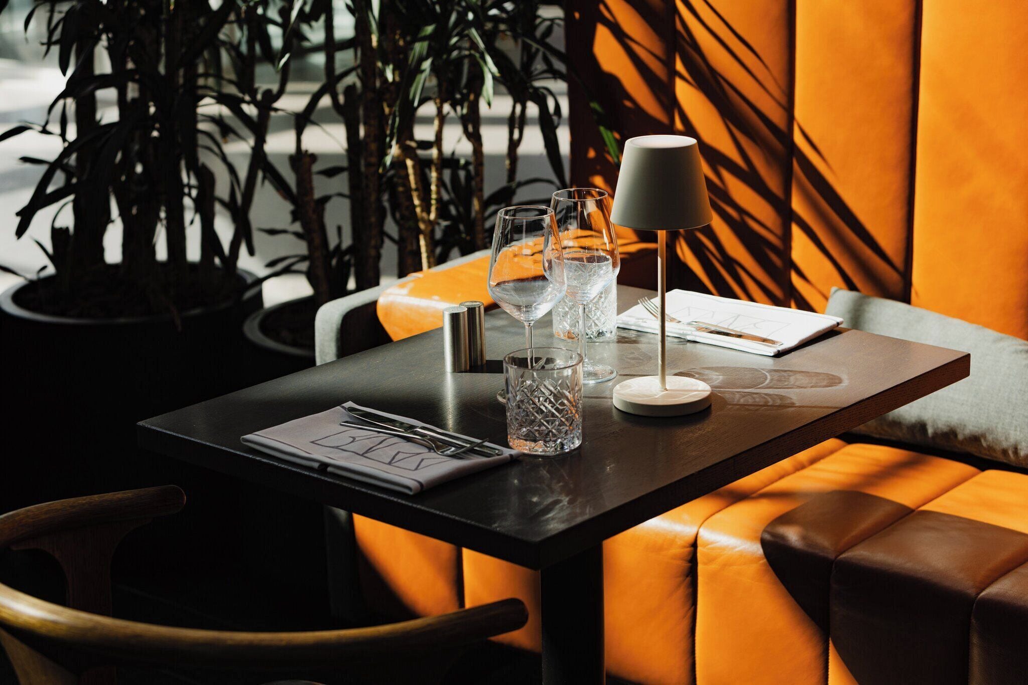 A table with a laptop, glasses, and a lamp, surrounded by orange cushioned seating.