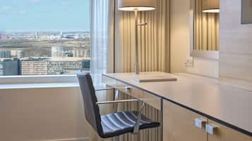 Une chambre d’hôtel moderne équipée d’un bureau, d’une chaise, d’une lampe et d’une grande fenêtre donnant sur la ville.