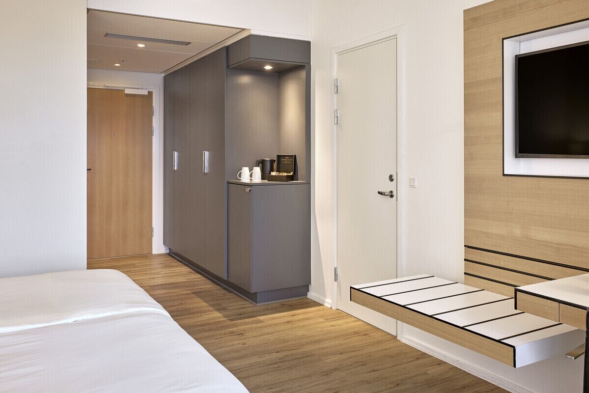 Una habitación de hotel moderna con cama, armario, televisor y un pequeño rincón de descanso.