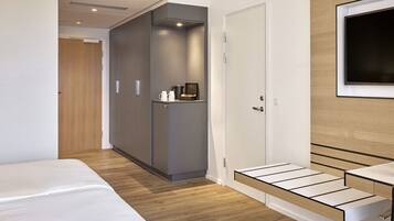 Una habitación de hotel moderna con cama, armario, televisor y un pequeño rincón de descanso.
