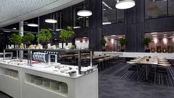 A modern dining area with a buffet setup, multiple tables, and potted plants.